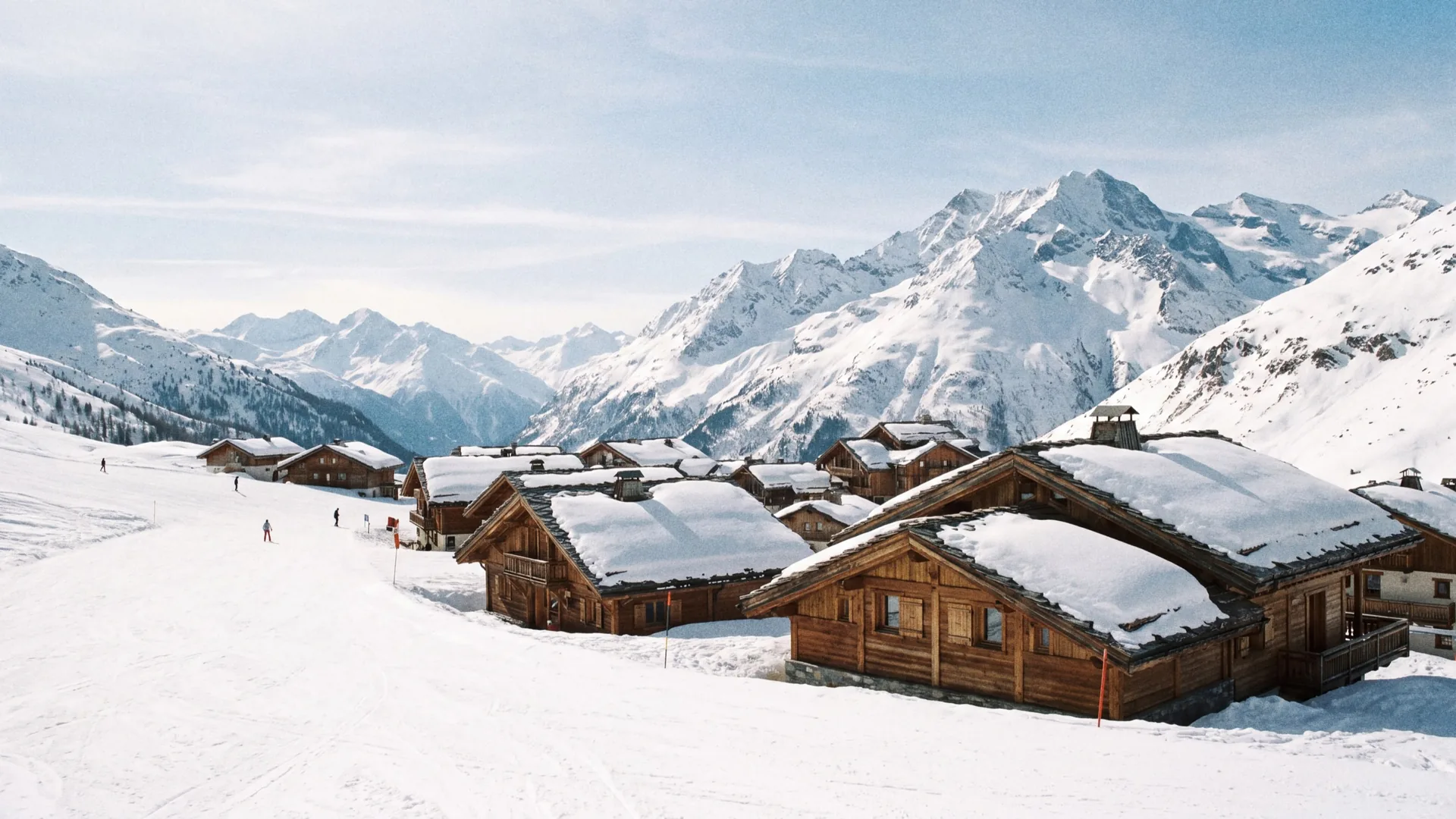 View across the ridge between the Courchevel and Méribel valleys on a clear winter day, with skiers on a wide piste in the foreground.