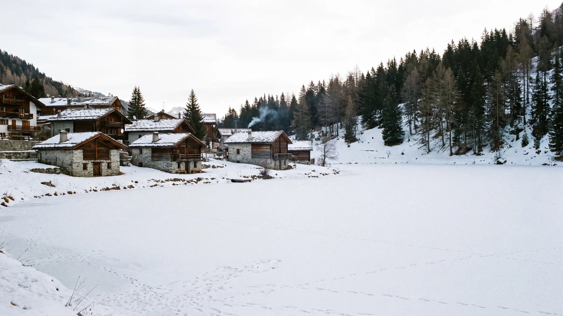 The frozen lake of Courchevel Le Praz in winter, with the village chalets, the chapel and the snowy forest rising behind.